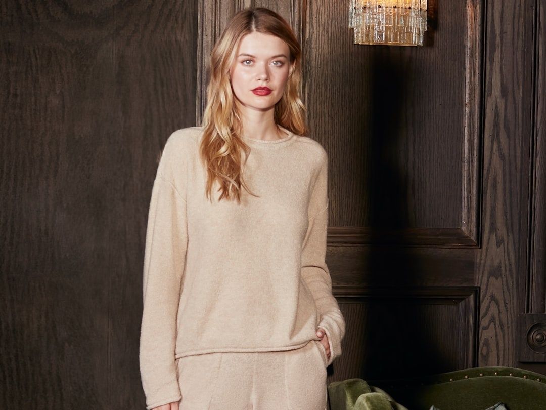 Model in een monochrome beige gebreide outfit voor een donkere houten wand